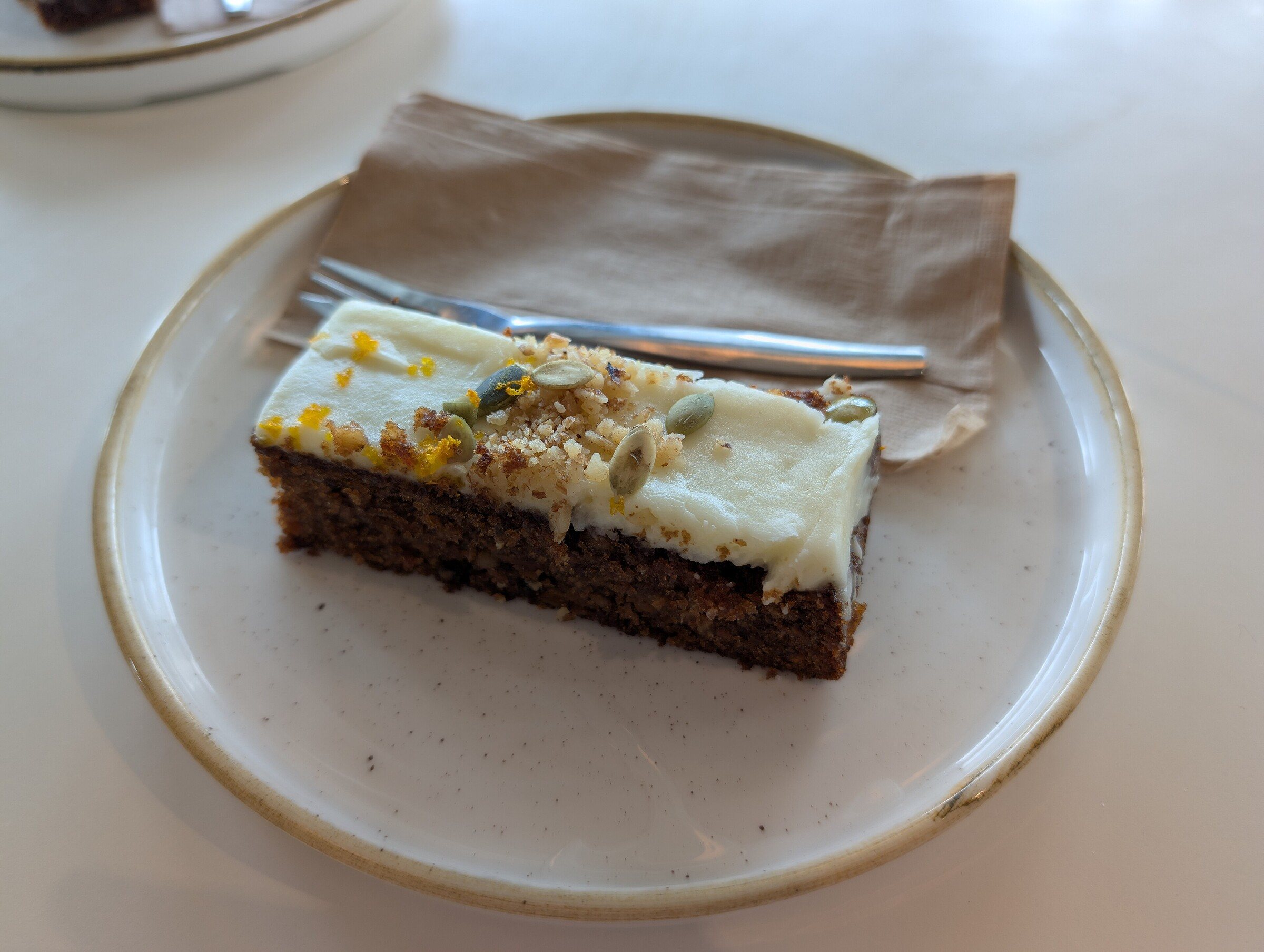 A slice of carrot cake with cream cheese frosting and walnuts on a ceramic plate