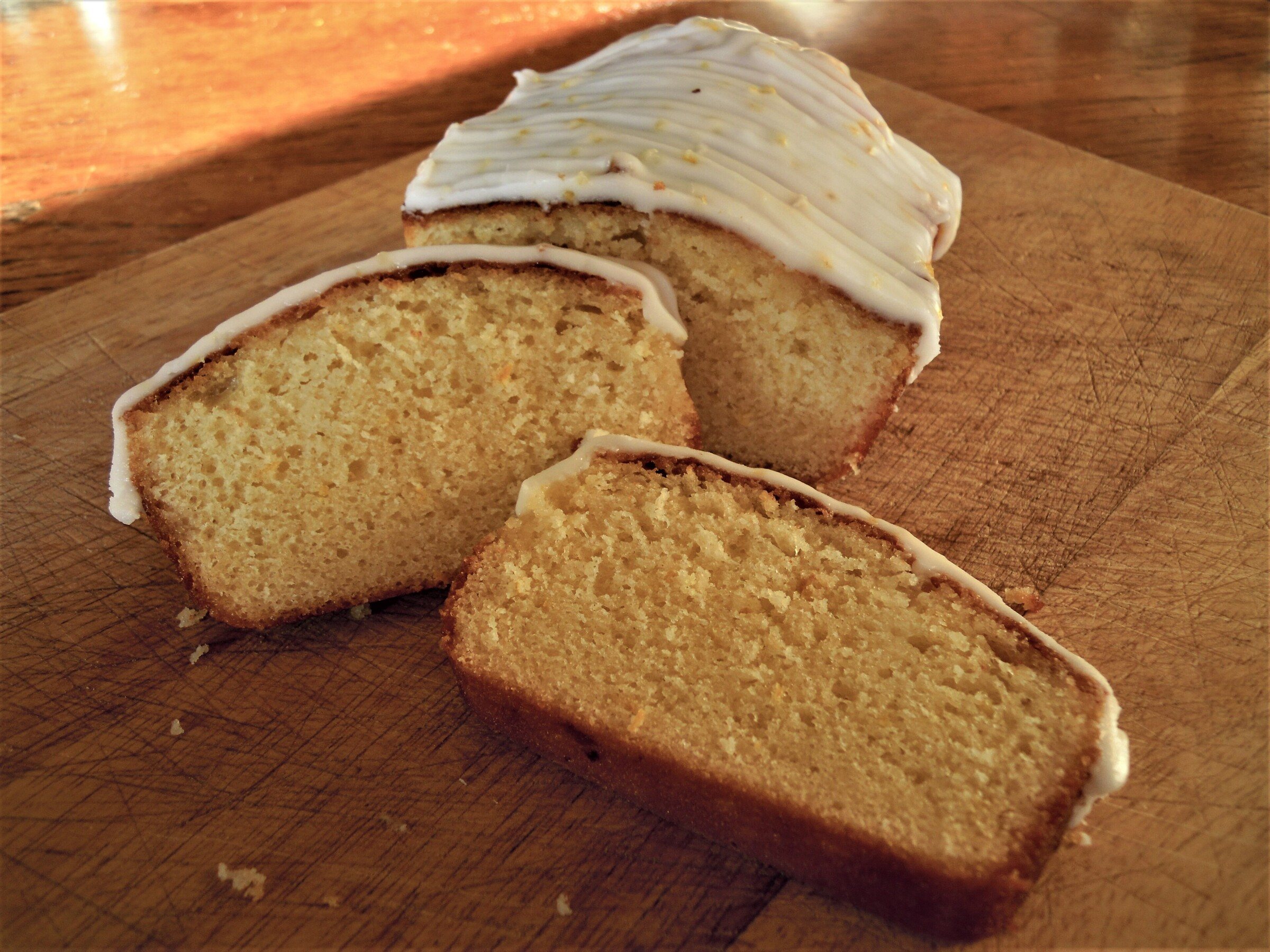 Slices of lemon drizzle loaf cake with white lemon icing on a wooden board