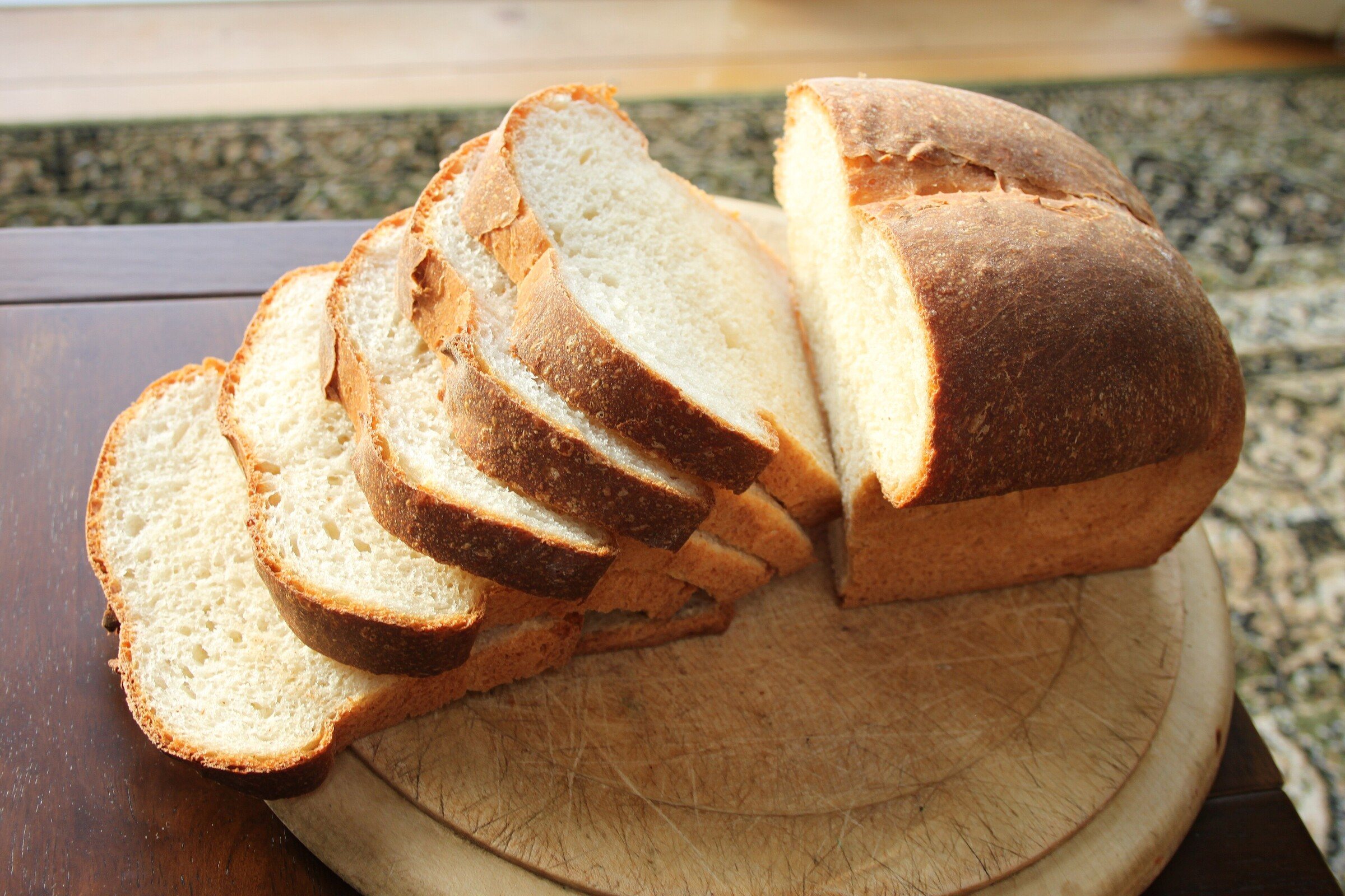 A homemade white loaf with several slices cut on a wooden board