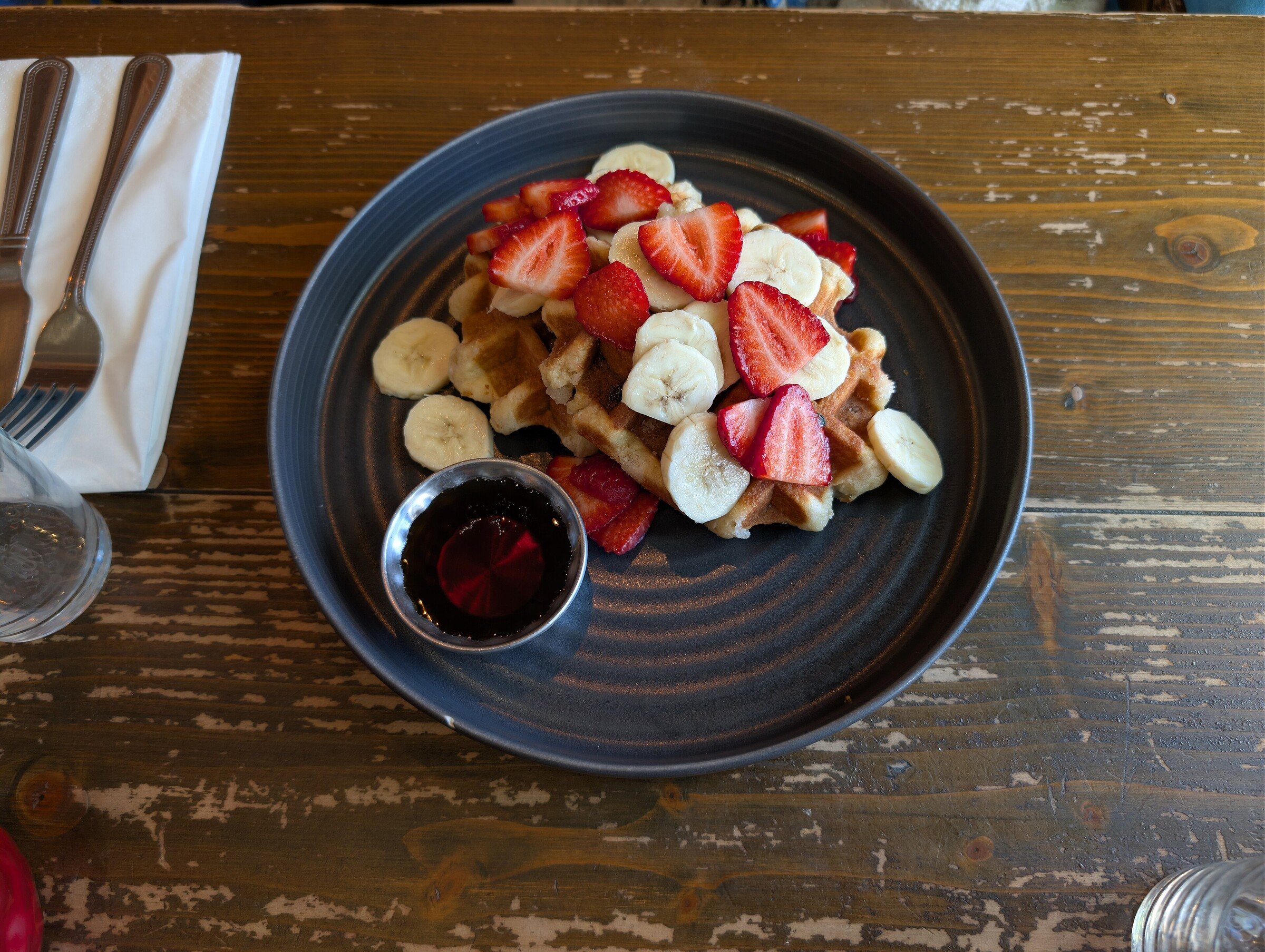 Waffles topped with strawberries and banana slices with a small dish of syrup